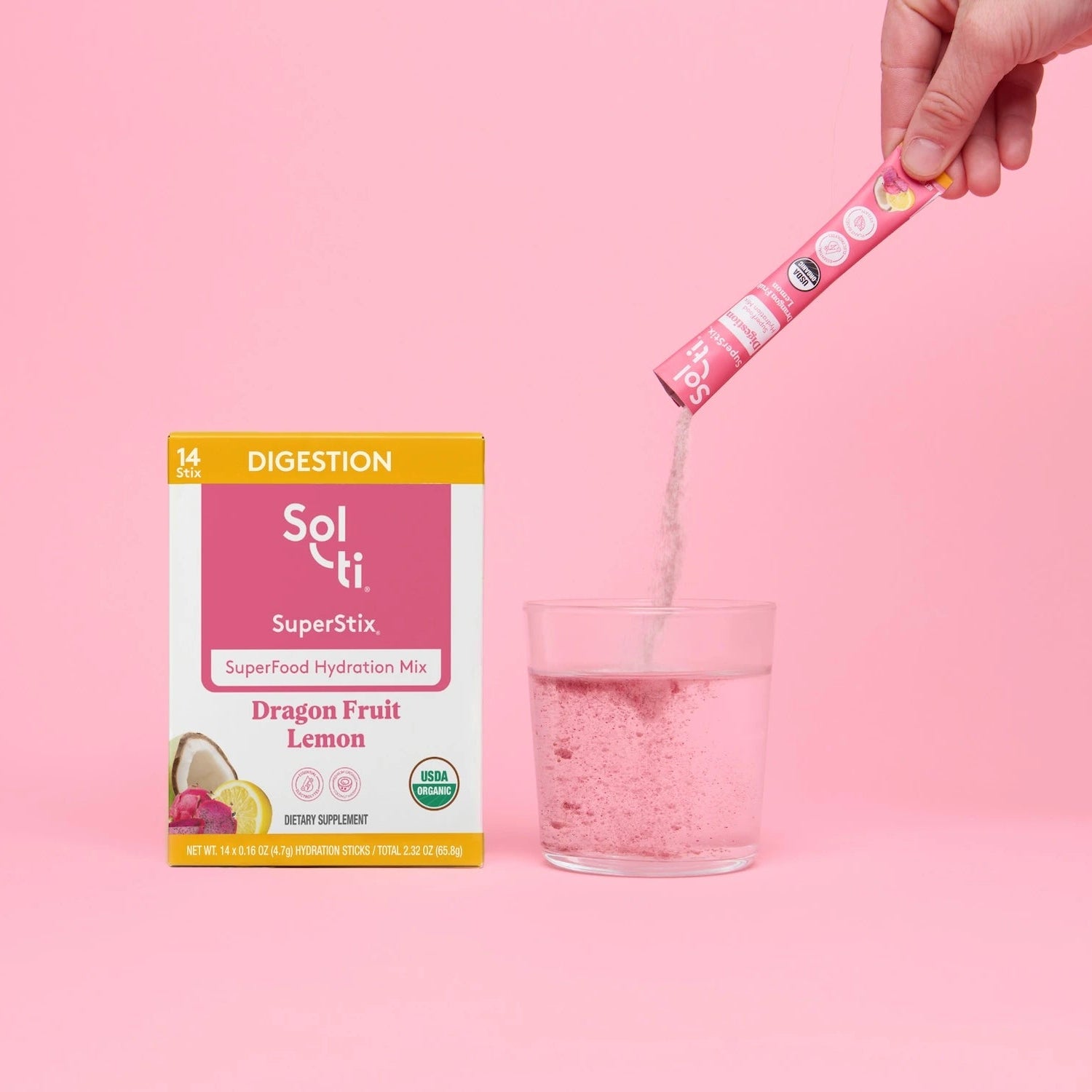 Hand pouring Sol-ti SuperStix hydration mix into a glass beside the product box