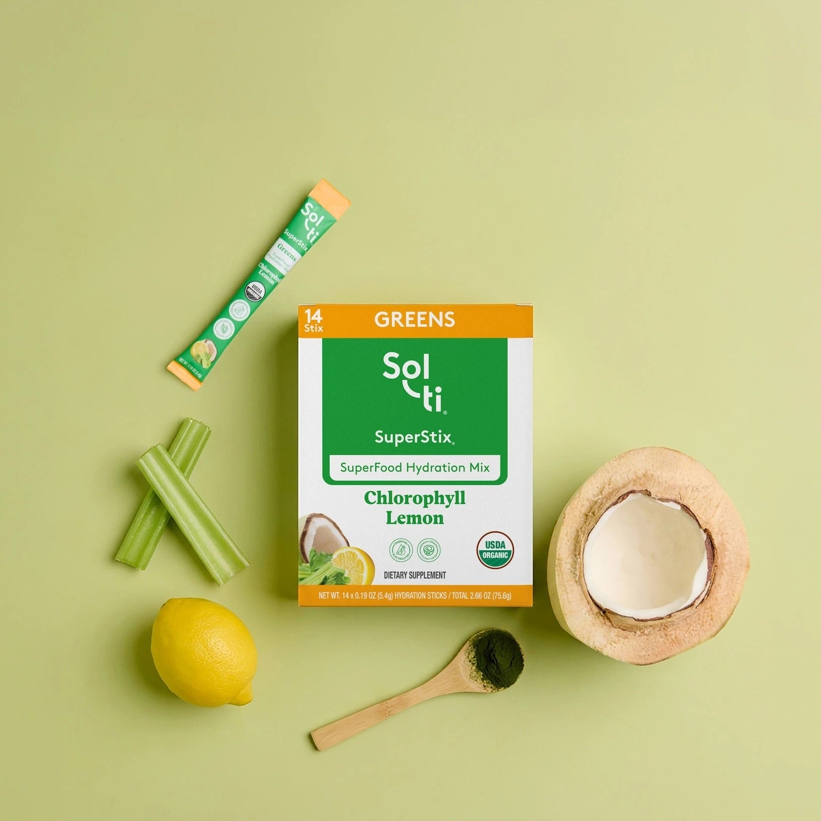 Sol-ti Greens SuperStix Chlorophyll Lemon hydration mix shown with a box, a single stick packet, celery stalks, a lemon, a coconut half, and a wooden spoon on a light green background.