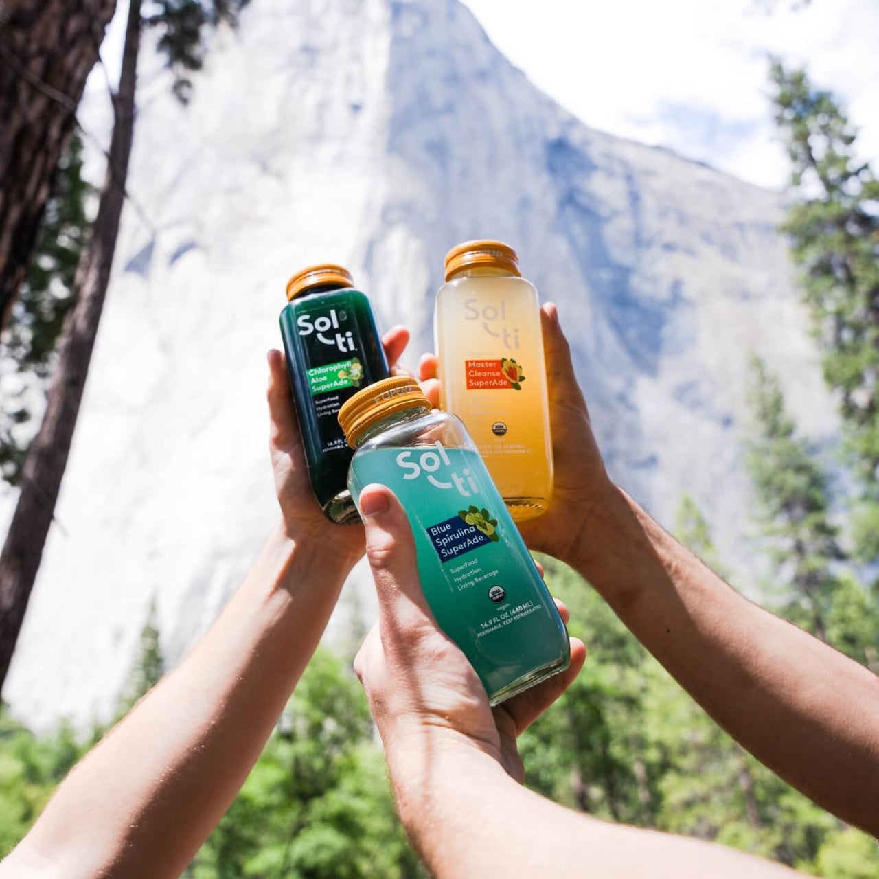 hands holding SuperAde bottles with a mountain behind