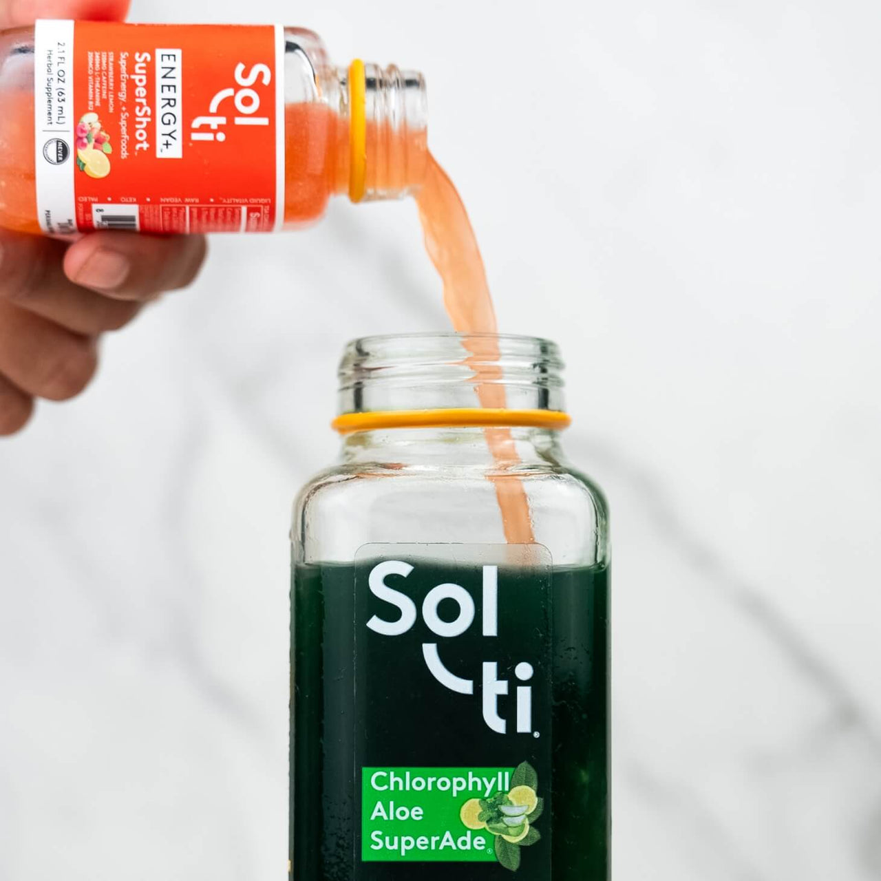 a hand pouring a ENERGY+ SuperShot into Chlorophyll Aloe SuperAde