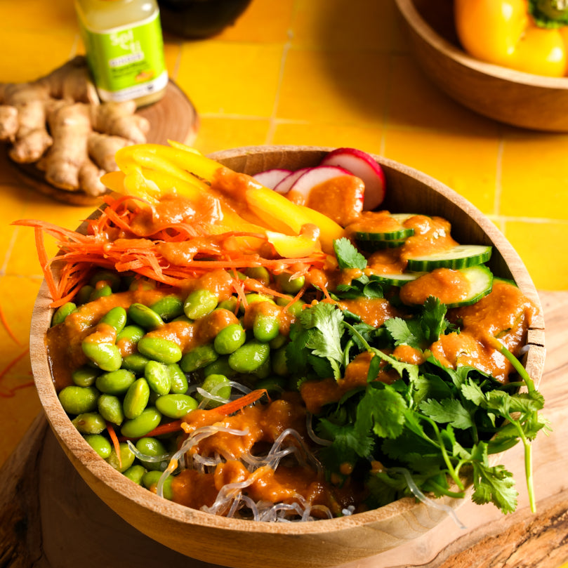 Spring Roll Bowl with various vegetables and kelp noodles with Bottle of GINGER SuperShot on a yellow background
