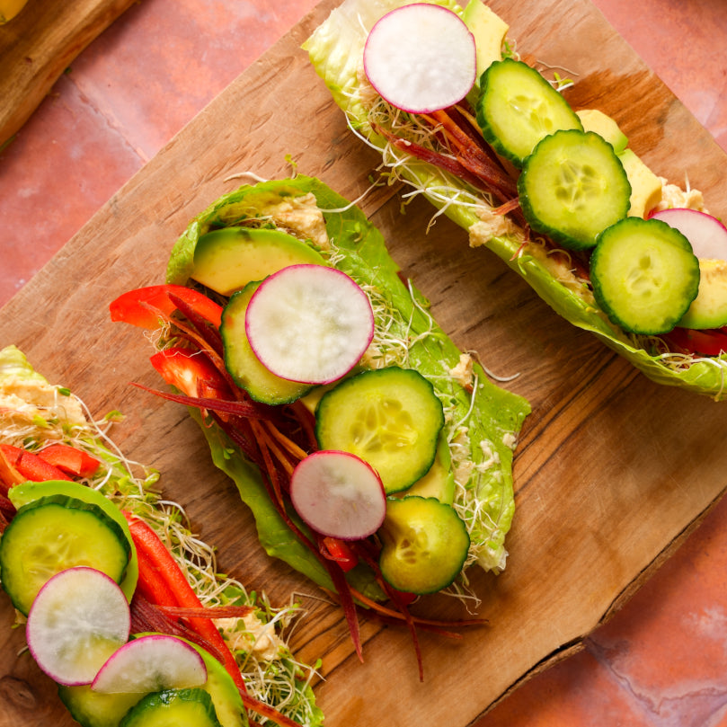 Veggie wraps with cucumbers, radishes, avocado and red peppers on a wooden board.