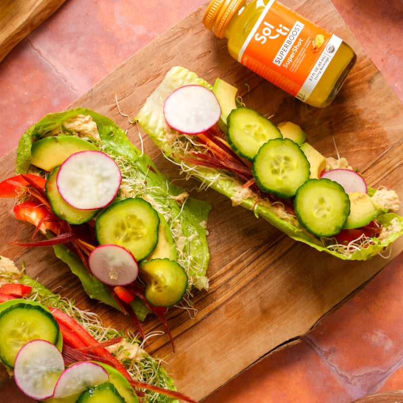 Three lettuce wraps with vegetables on a wooden board with a Bottle of SUPERBOOST SuperShot.