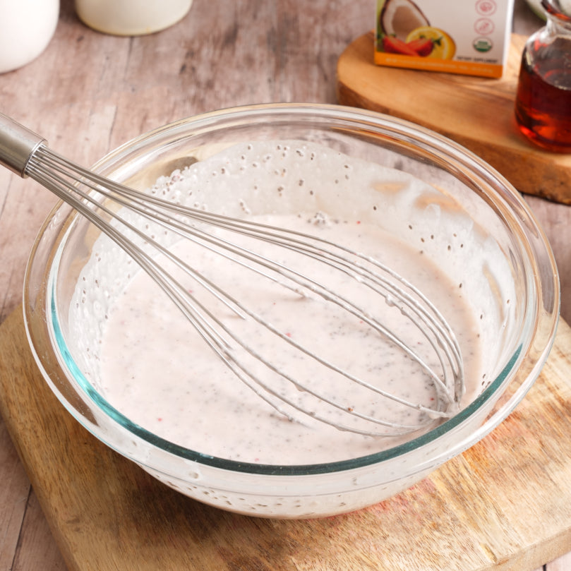 Glass bowl with creamy mixture and whisk on a wooden surface