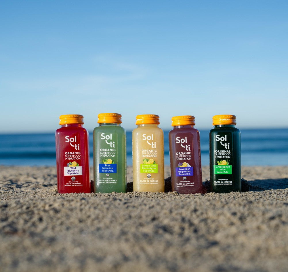 Five So-ti bottles on a sandy beach with a clear blue sky. 