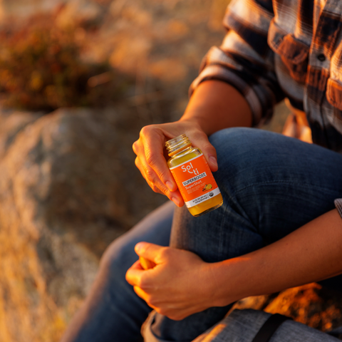 Sol-ti SUPERBOOST SuperShot bottle held by person, angled front label, warm background