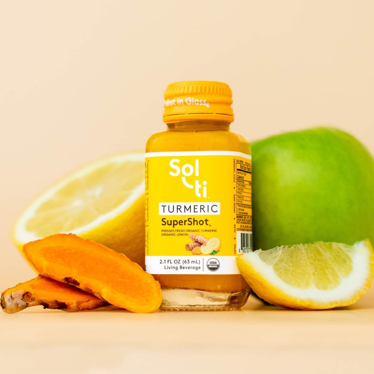 a TURMERIC SuperShot bottle with an apple, turmeric root and lemon slices