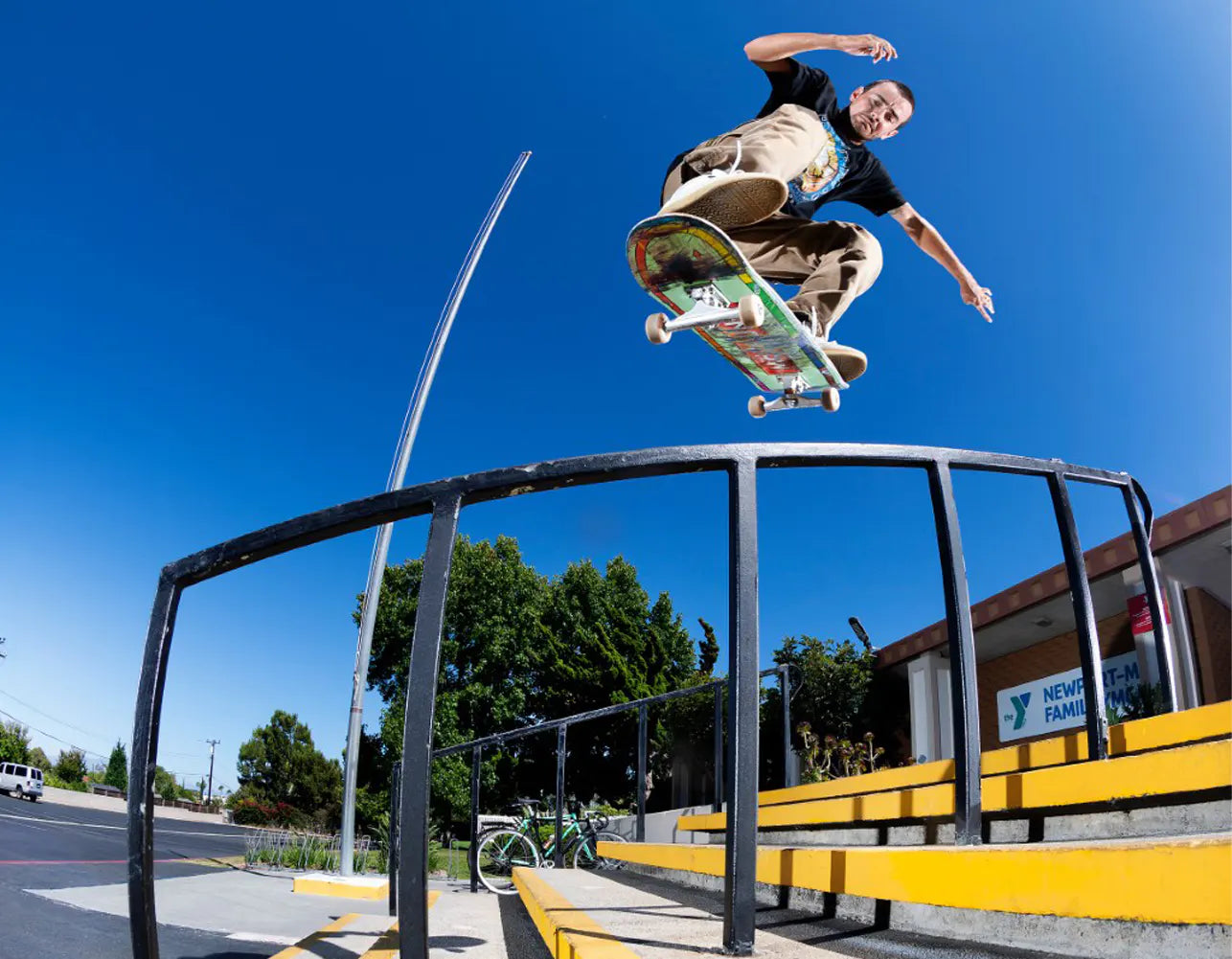 Trevor McClung mid-air performing a trick above a black metal rail in an outdoor urban setting 