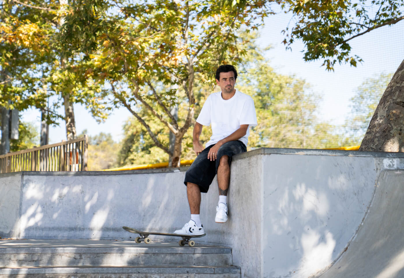 Trevor McClung sits on a concrete skatepark ramp with a skateboard on the steps below