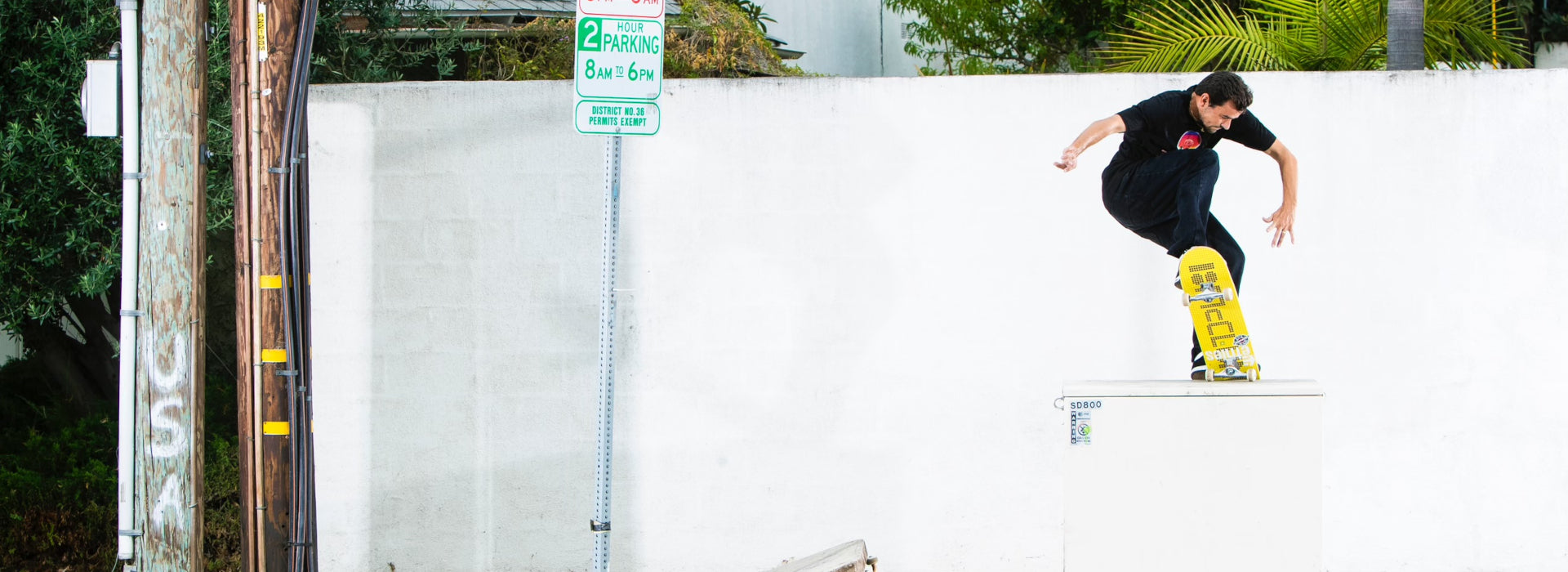 Trevor McClung performs a trick on a yellow skateboard while balancing on top of a white utility box