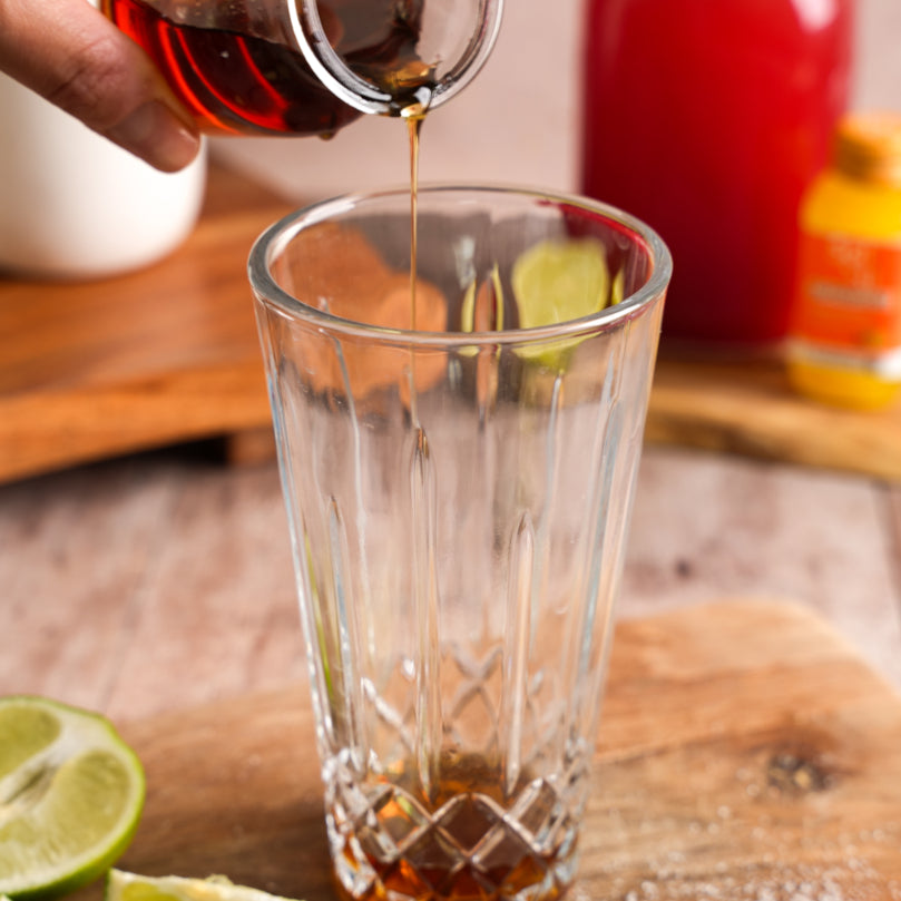 Pouring a Maple Syrup into a clear glass with lime wedges on a wooden surface.