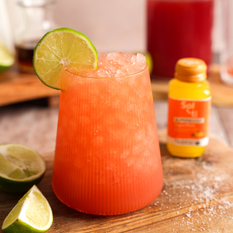 Watermelon Refresher with a lime slice on a wooden surface with a bottle of Sol-ti SUPERBOOST™ SuperShot® in the background.