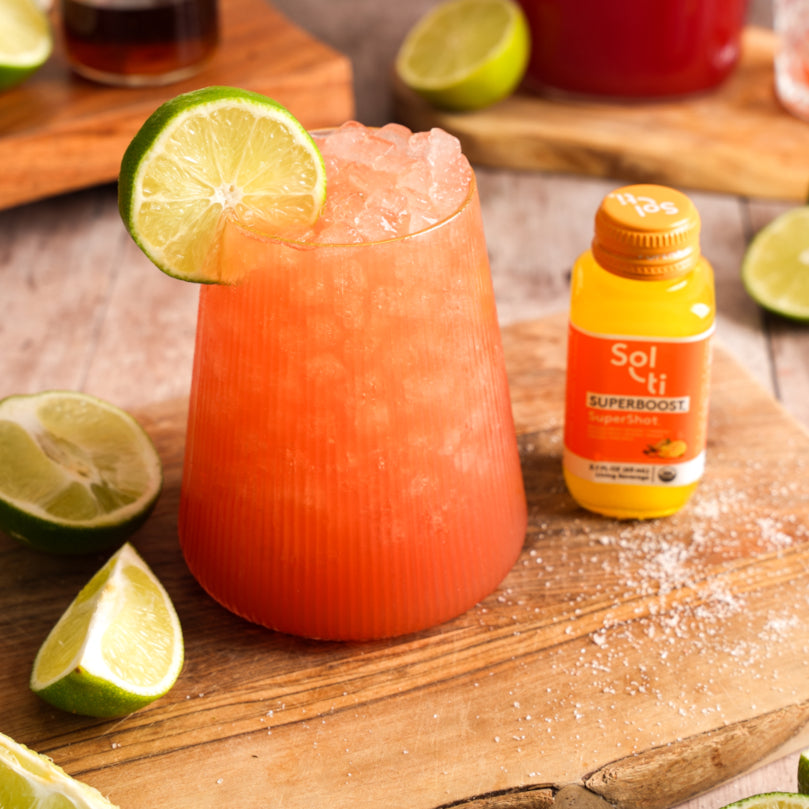 Watermelon Refresher with lime garnish on a wooden board next to a bottle of Sol-ti SUPERBOOST™ SuperShot®.