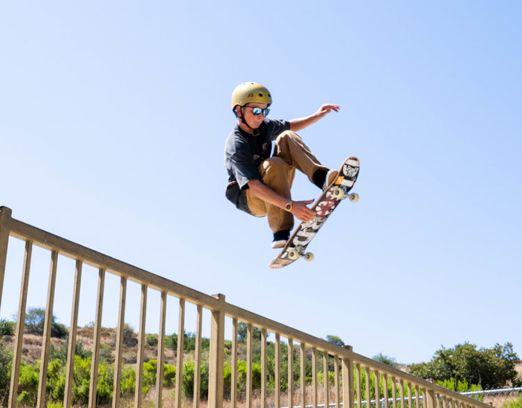Wyatt Hammond performs a trick mid-air above a metal railing outdoors under a clear blue sky