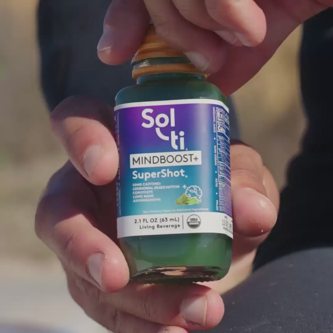Close-up of a Sol-ti MINDBOOST+ SuperShot bottle, followed by a man in a wetsuit drinking it, then surfing large waves with energetic jumps and turns; finishes on an orange screen with the Sol-ti logo.