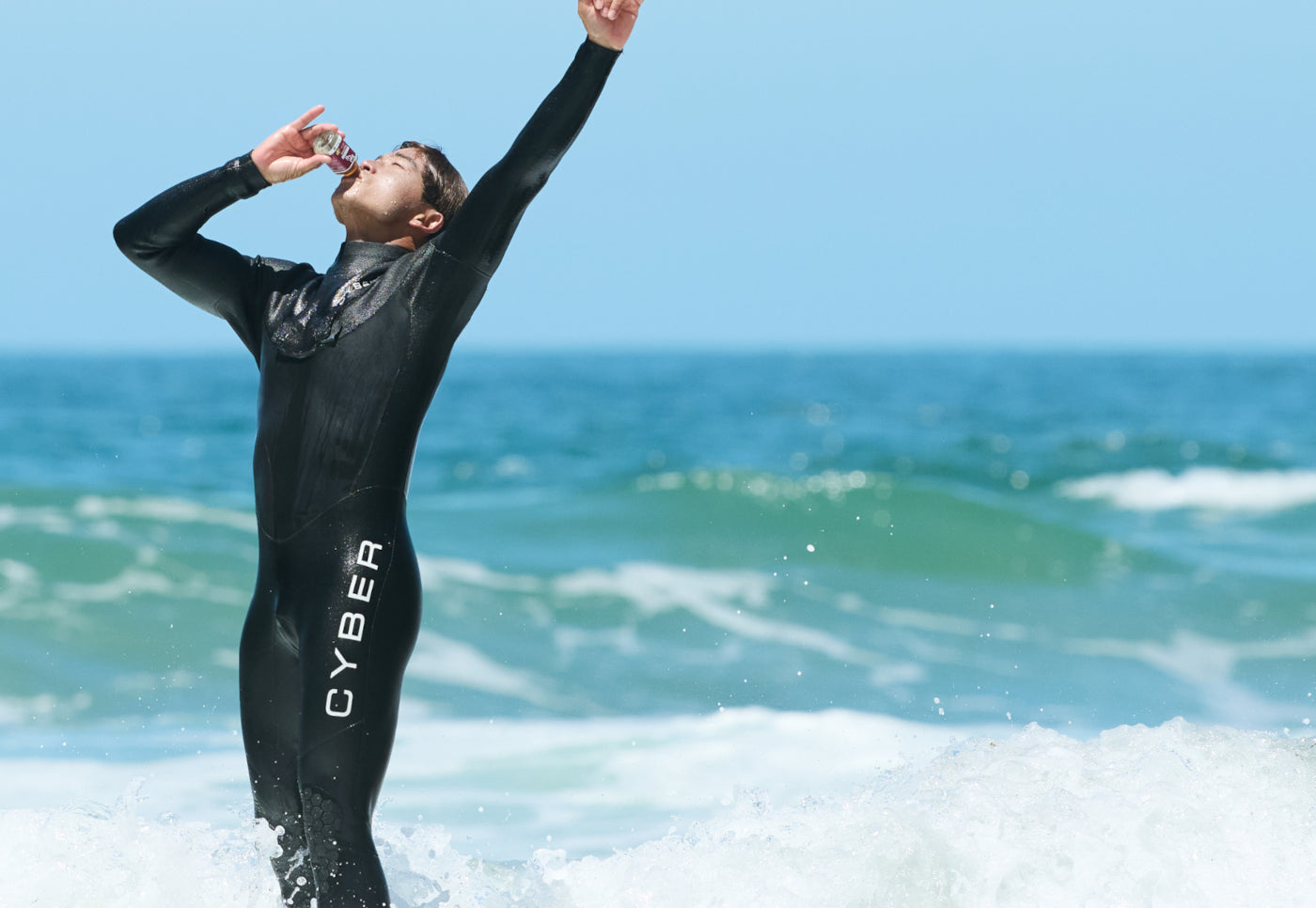 Person in a wetsuit standing in the ocean drinking a Sol-ti SuperShot.