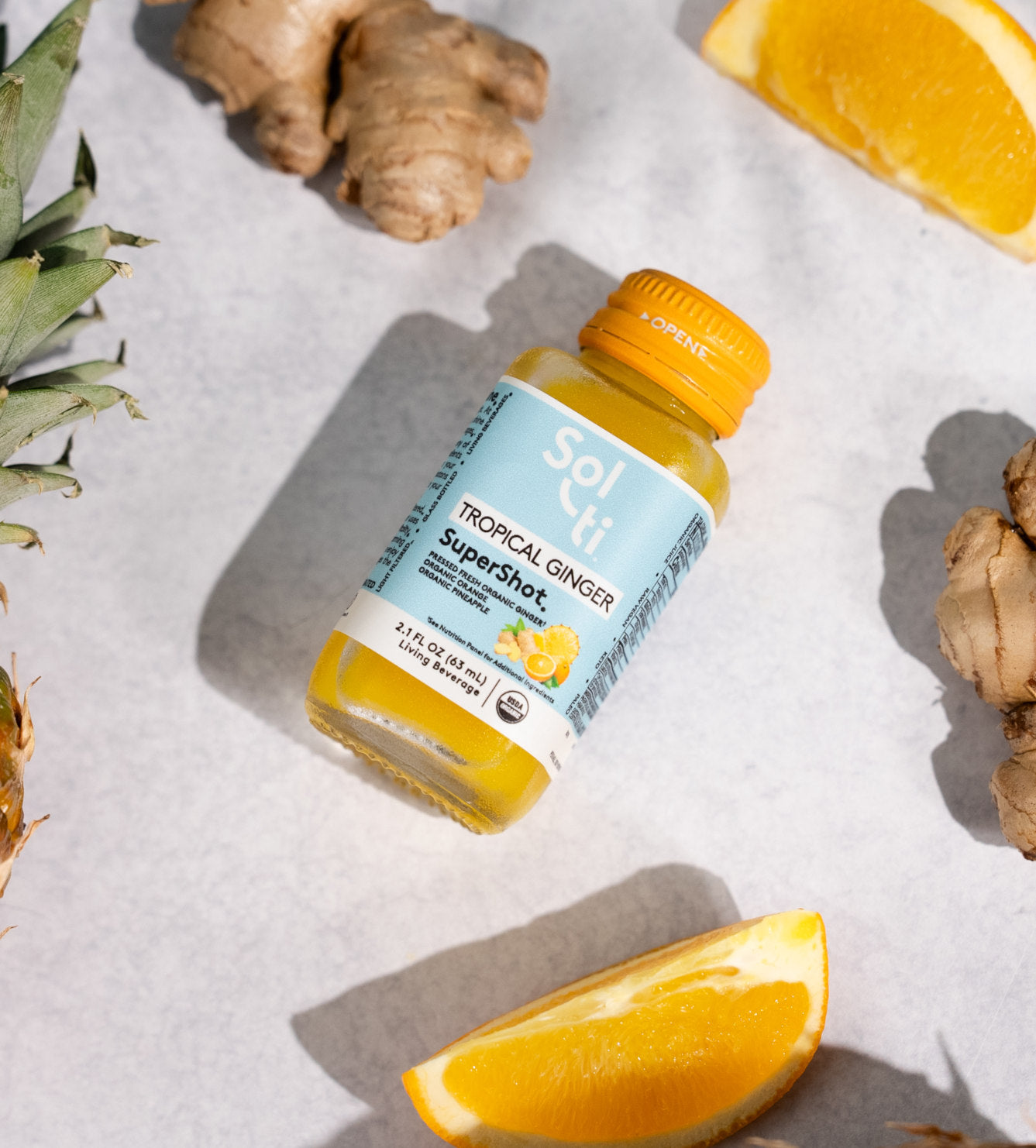 TROPICAL GINGER SuperShot bottle with  front label on light background with ginger root, pineapple and lemon slices 